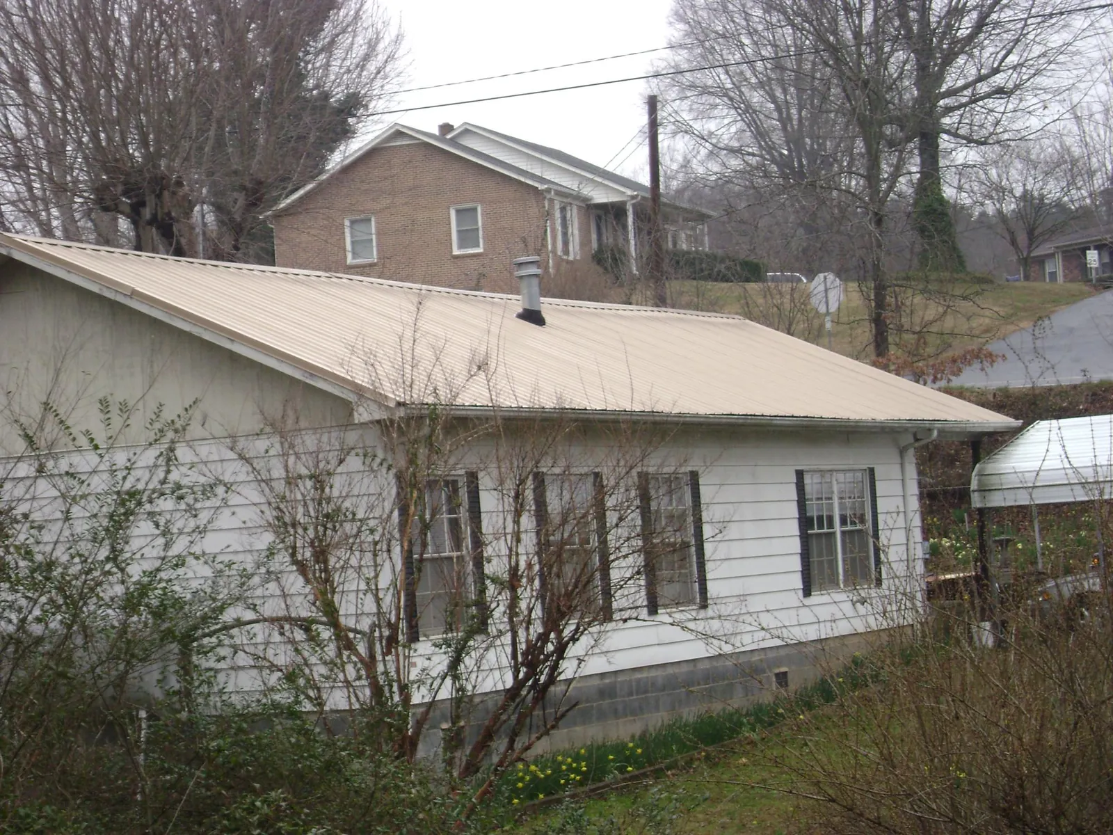 Tan metal roof on a white sided house set into a hillside — Commercial Roofing by Roofing Brothers in Naples